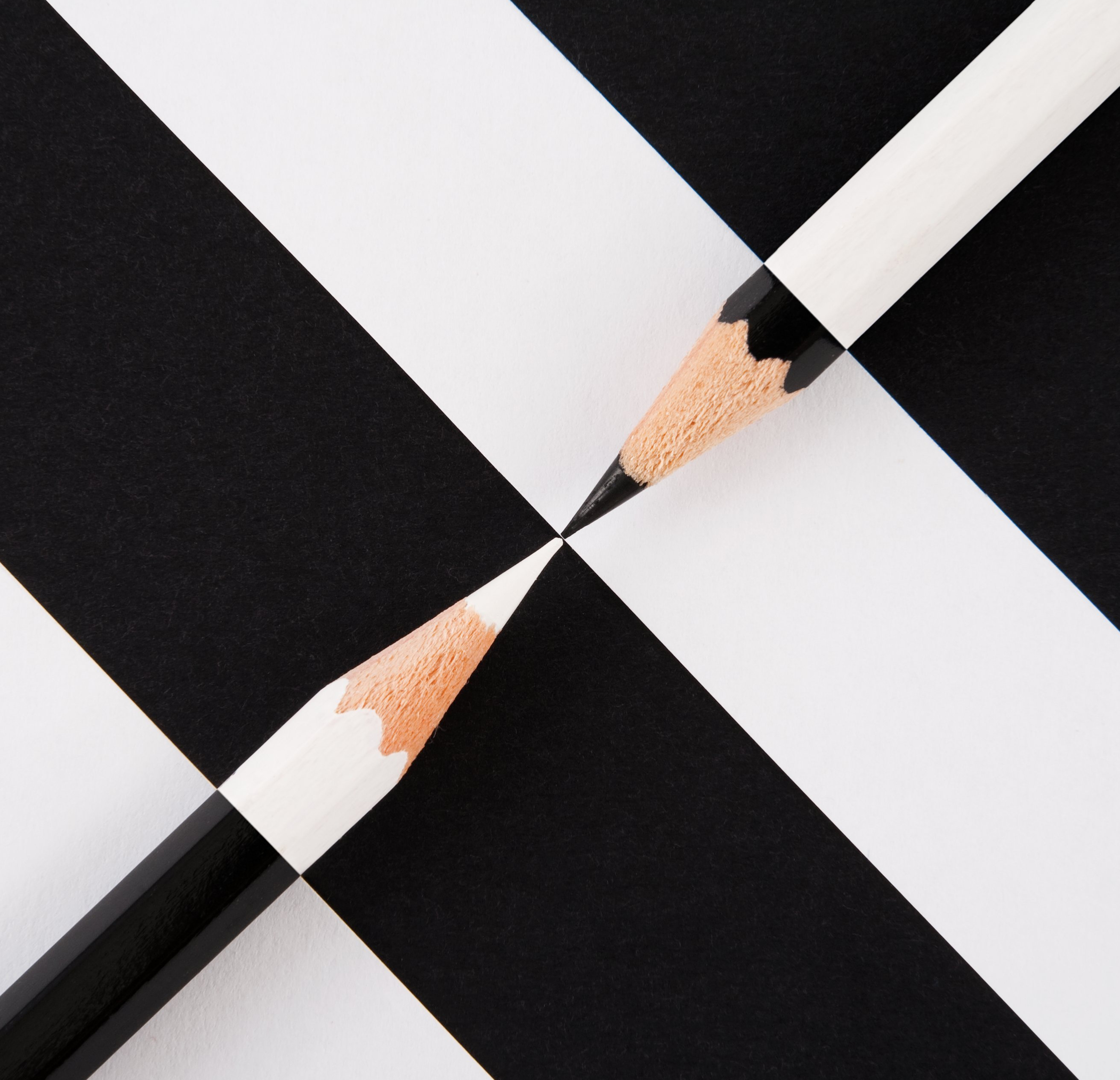 A black pencil and a white pencil pointing at each other over a black and white background