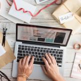 A person typing on a laptop surrounded by craft supplies and scissors