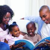 A mother and father reading a book to a girl and boy
