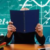 Kid reading a book in front of a blackboard