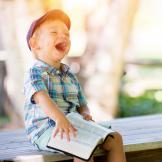 An image of a child, reading and laughing, outdoors
